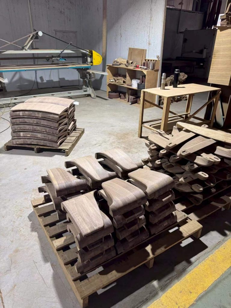 Curved solid black walnut chair components stacked on pallets in the Villa furniture workshop
