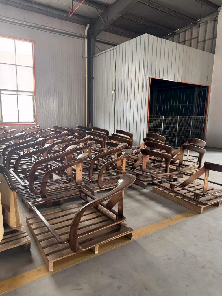 Solid walnut lounge chair frames in rows beside the spray booth for hand-rubbed oil finishing